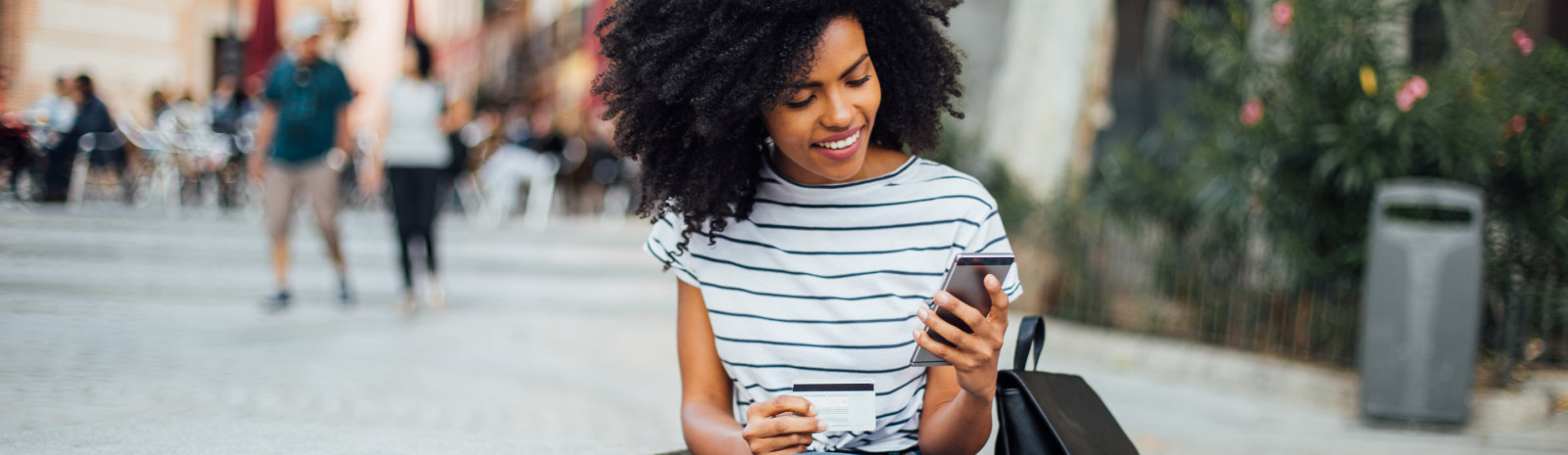 Young woman holds phone and card as she sits outdoors.