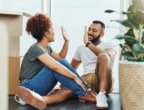 Young couple high five in room surrounded by moving boxes.