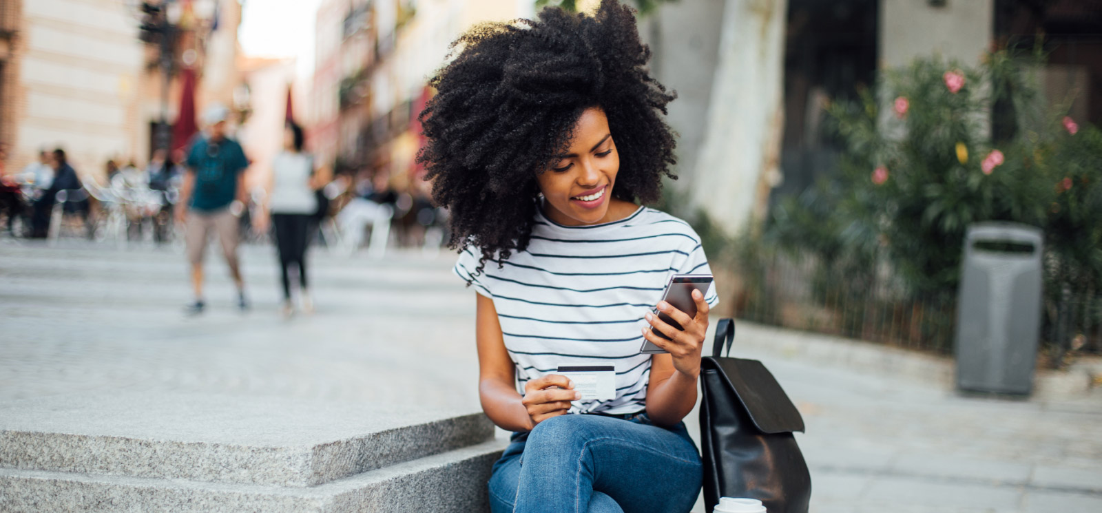 Woman sitting outside holding phone and card in hand.